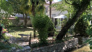 A stone wall with a small stream, surrounded by lush greenery and a building with a tiled roof in the background. - Family home in the heart of the Eure valley - 10 people - 5 bedrooms (Breuilpont)