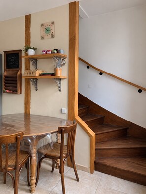 Un espace repas avec une table et des chaises en bois, un panneau noir et un escalier.