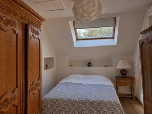 Une chambre avec un puits de lumière, un lit recouvert d’une couvre-lit à motifs, une table de chevet avec une lampe et des meubles en bois.