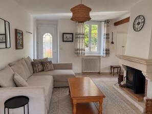 Un salon comprenant un canapé, une table en bois, une cheminée et une grande fenêtre avec des rideaux.