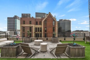 Una terraza en la azotea con un edificio de ladrillo, mobiliario exterior y el horizonte de la ciudad al fondo.