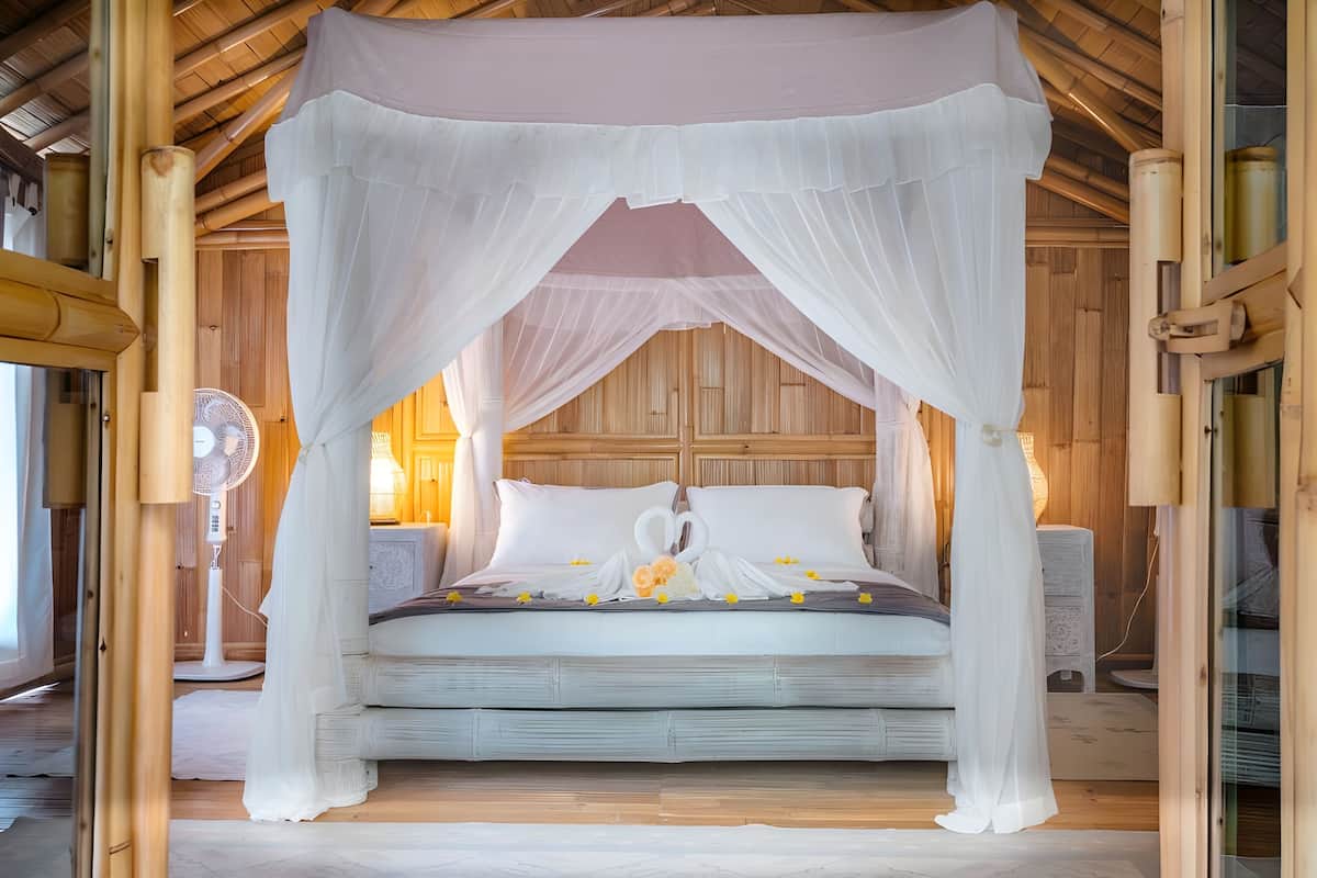Una cama con dosel, paredes de madera y un ventilador junto a la cama.