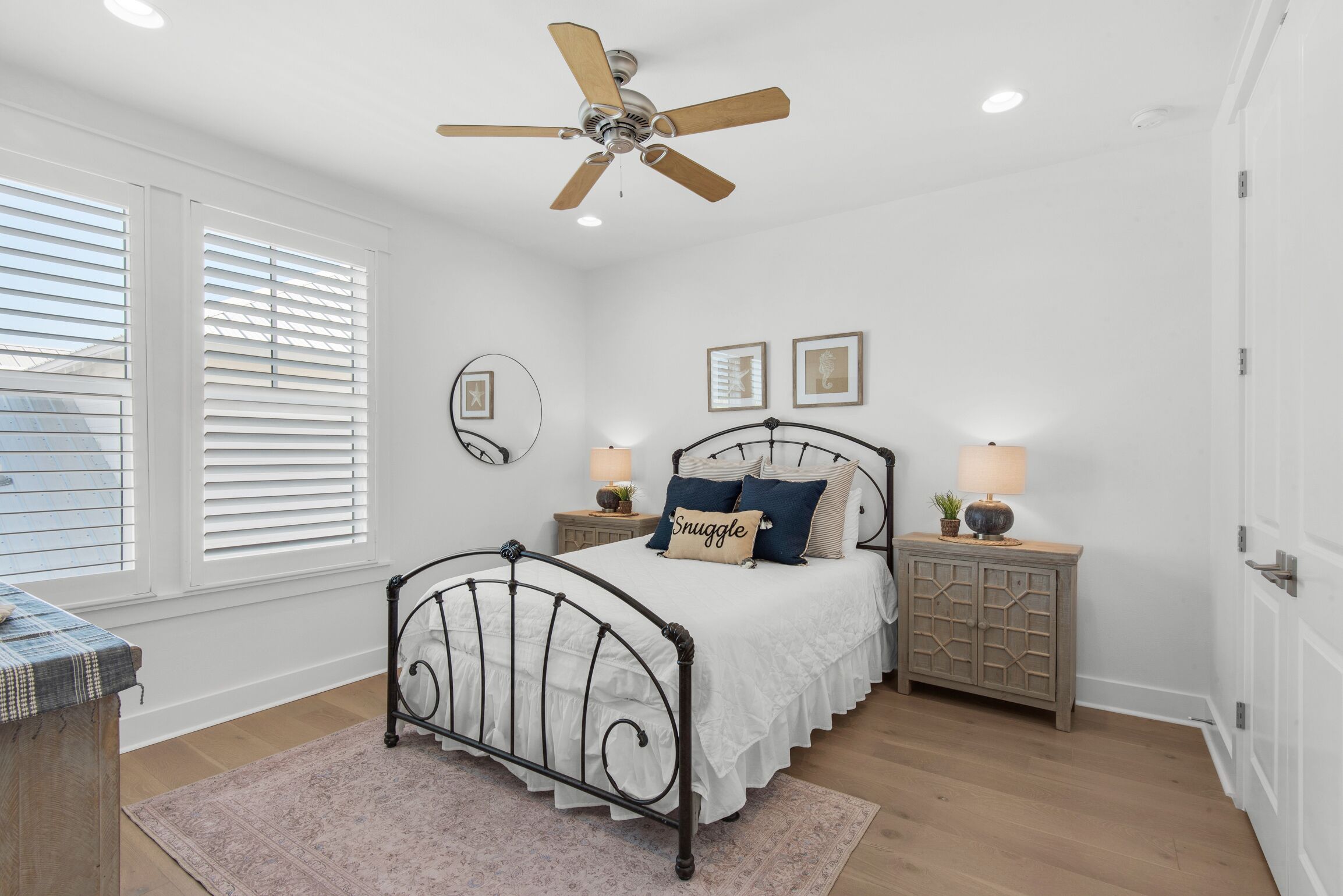 Une chambre à coucher comprenant un lit, des tables de chevet, un ventilateur de plafond et une fenêtre avec des stores.