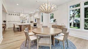 A modern kitchen with white cabinetry, a central island, and a round dining table with chairs.