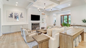 A spacious living room with a fireplace, a dining area with wooden furniture, and a large window offering a view of greenery.