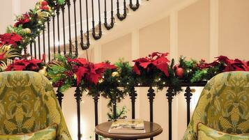 A staircase decorated with Christmas garlands and poinsettias, flanked by two green upholstered chairs and a small table.
