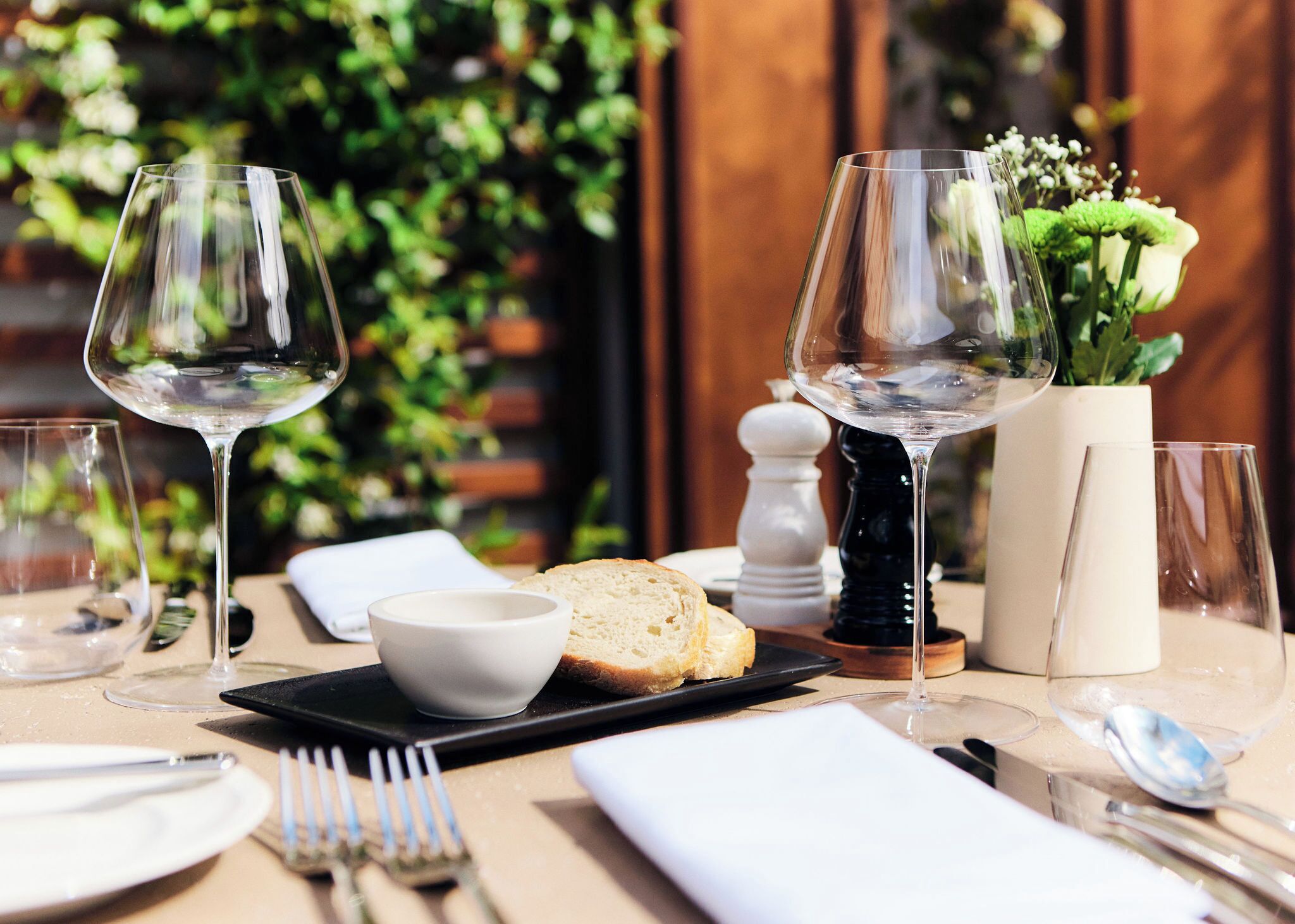 A table set for a meal with wine glasses, a bread roll, a bowl, and a vase with flowers.