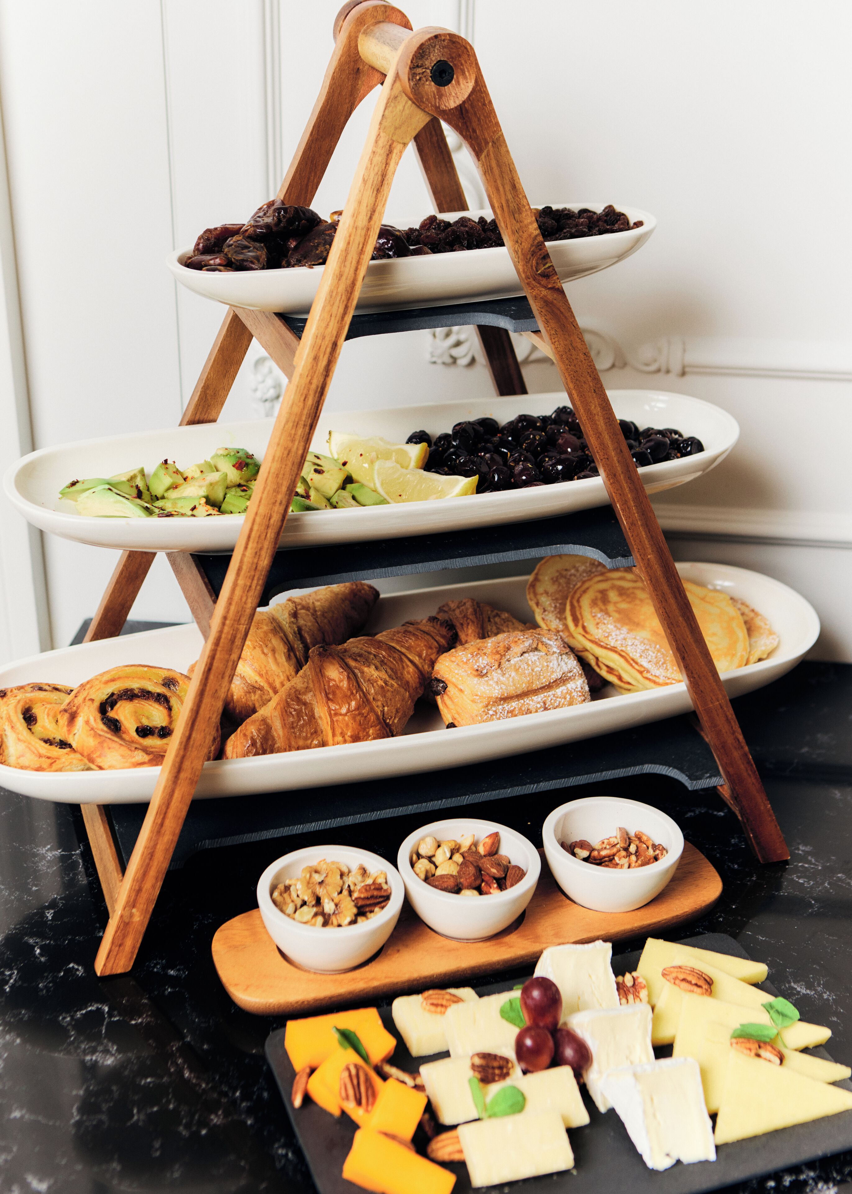 A multi-tiered wooden stand holding plates of pastries, fruits, and nuts.