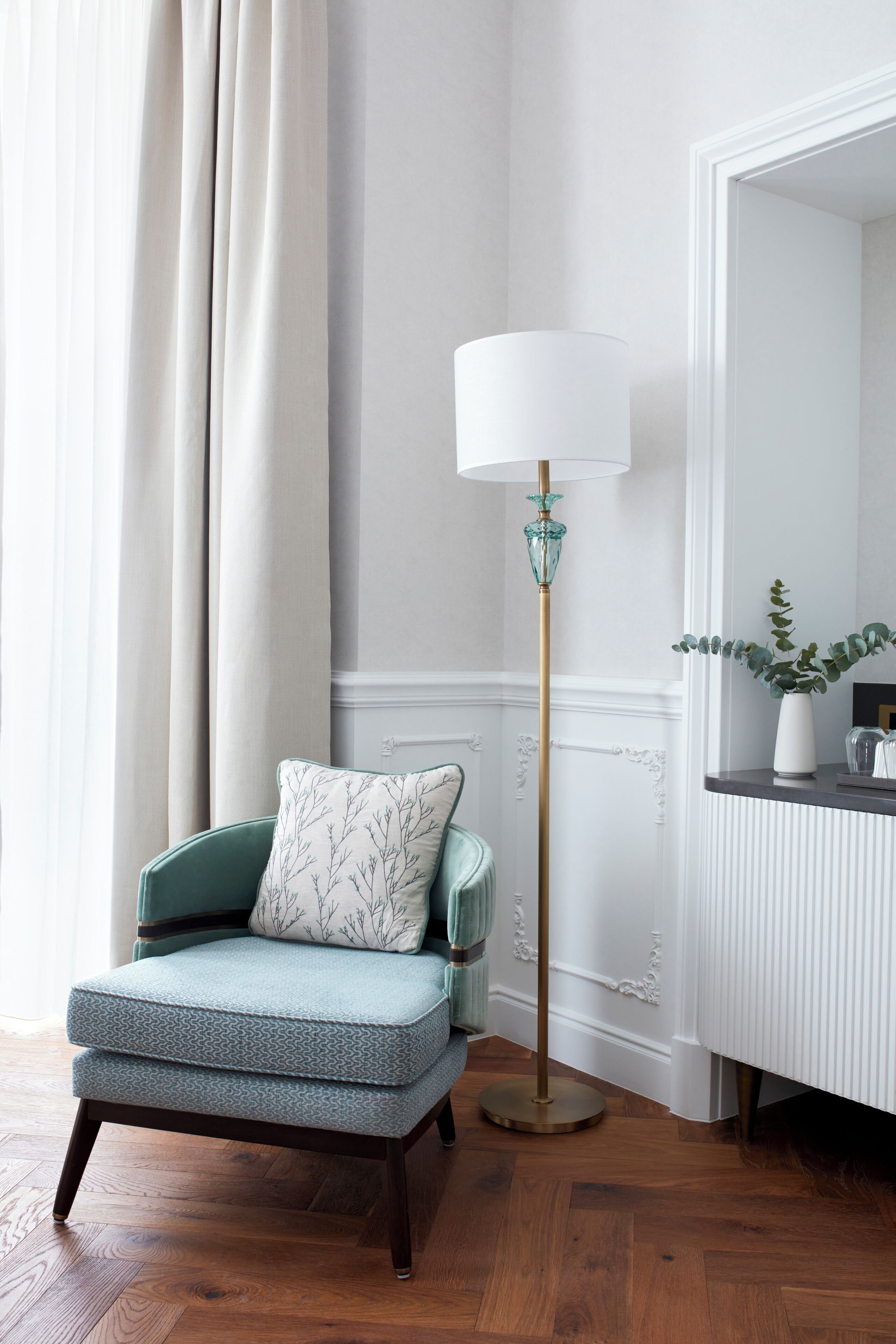 Ein Zimmer mit einem grünen, gepolsterten Sessel, einer Stehlampe und einem Spiegel an der Wand.