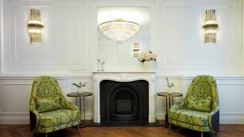 A room with a fireplace, two armchairs, a chandelier, and wall sconces.