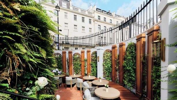 A courtyard with wooden benches and tables, surrounded by lush greenery and a wrought iron fence. - 2 Chesham Hotel (London)