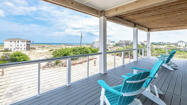 Una terraza techada con barandas de madera y dos sillas Adirondack turquesa.