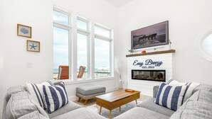 Una sala de estar moderna con chimenea, ventanas amplias y vista al océano.