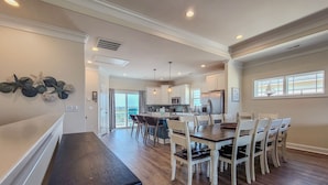 Una cocina amplia con una isla central, muebles blancos y una zona de comedor con mesa y sillas de madera.