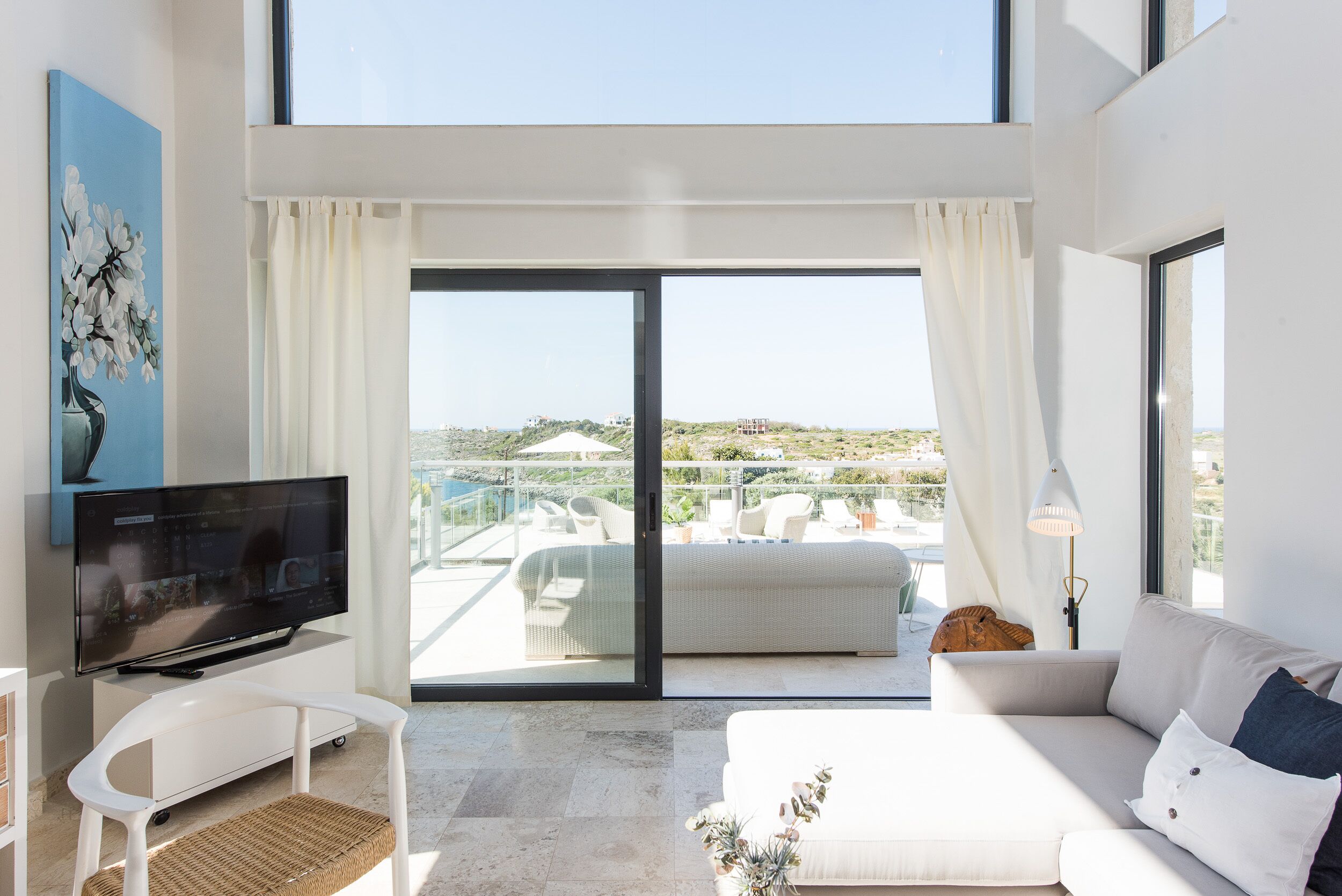 Una habitación de hotel moderna con un amplio ventanal corredero que da a un balcón con mobiliario exterior.