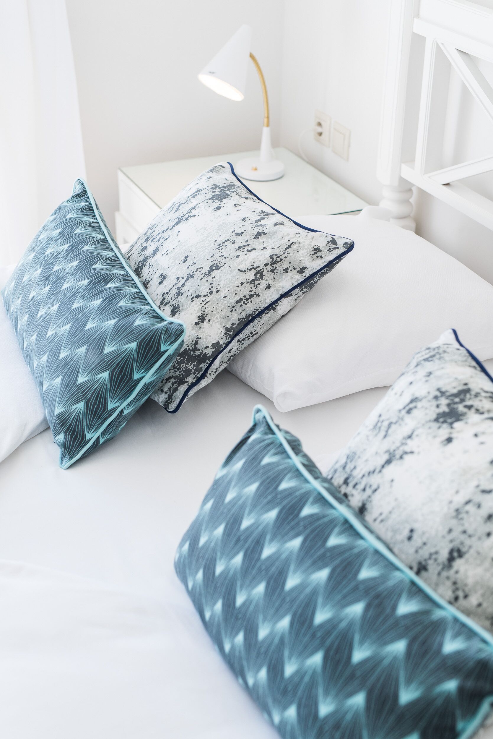A neatly arranged bed with patterned pillows and a bedside table with a lamp.