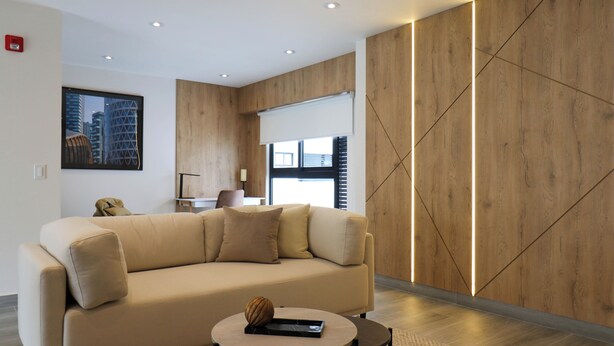 A modern living room with a beige sofa, a round coffee table, and a wooden accent wall. - Caster by Wynwood House (Lima)