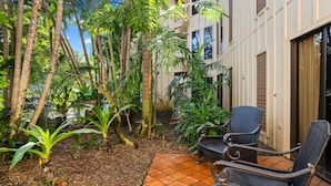 An outdoor area with a tiled patio, wicker furniture, and various tropical plants. - Waikomo Stream Villas 100 | Tropical Poipu Retreat Near Beach (Koloa)