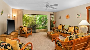 A room with wicker furniture, a ceiling fan, a TV, and a view of greenery through the glass door. - Waikomo Stream Villas 100 | Tropical Poipu Retreat Near Beach (Koloa)