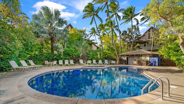 A circular pool surrounded by lounge chairs and palm trees, with a stone building in the background. - Waikomo Stream Villas 100 | Tropical Poipu Retreat Near Beach (Koloa)