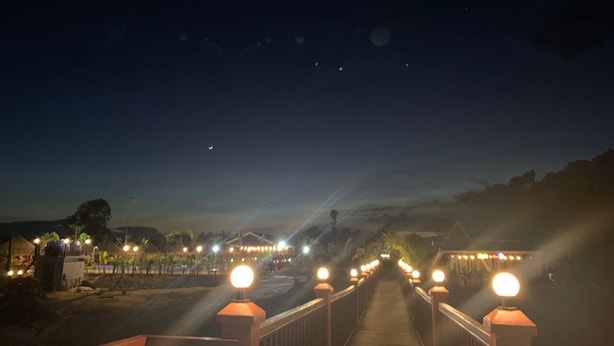 A wooden bridge with illuminated posts leading to a building with lights. - I AM Koh Ker (Kuleaen)