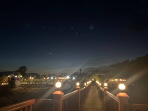 A wooden bridge with illuminated posts leading to a building with lights. - I AM Koh Ker (Kuleaen)