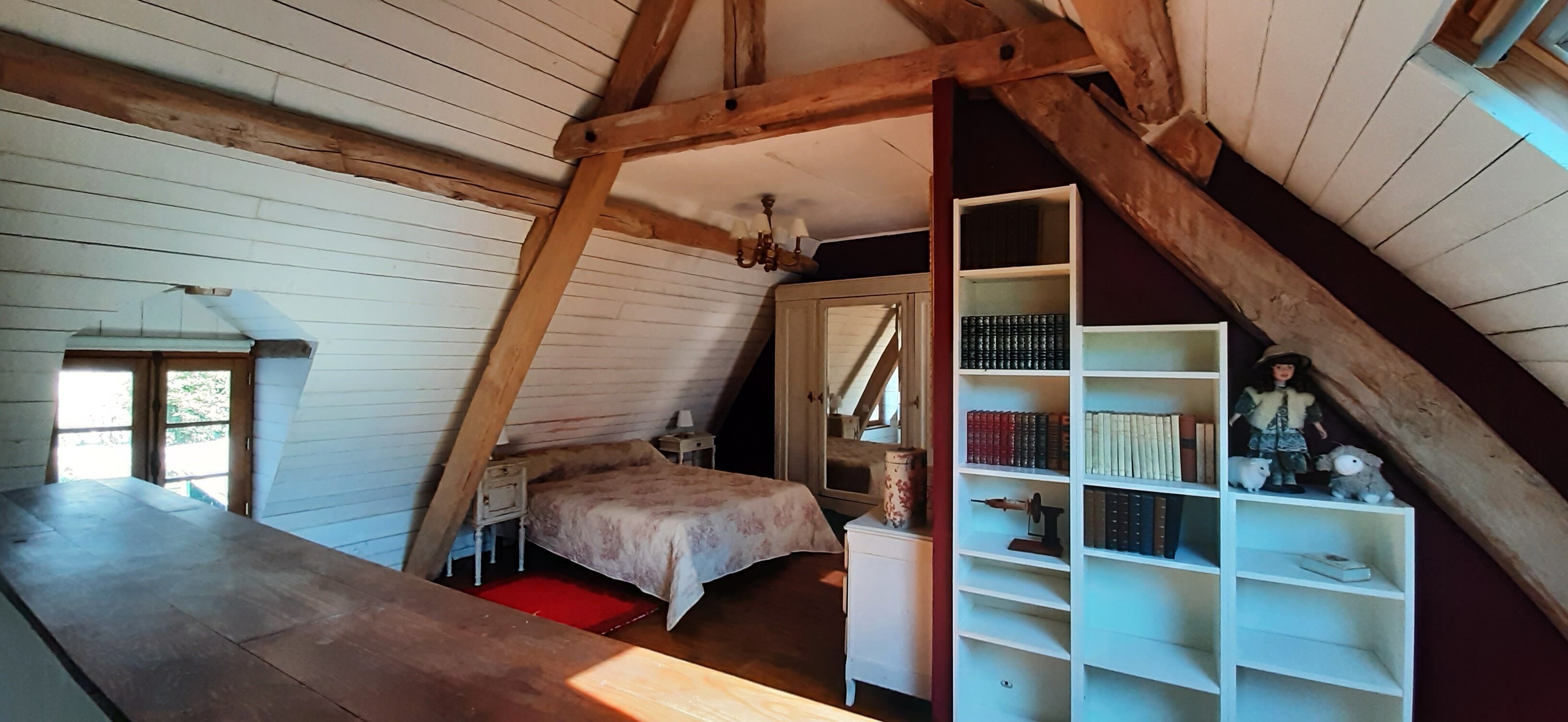 Een knus slaapkamer op zolder met houten plafond, een bed, nachtkastje, boekenkast en een klein tafeltje.
