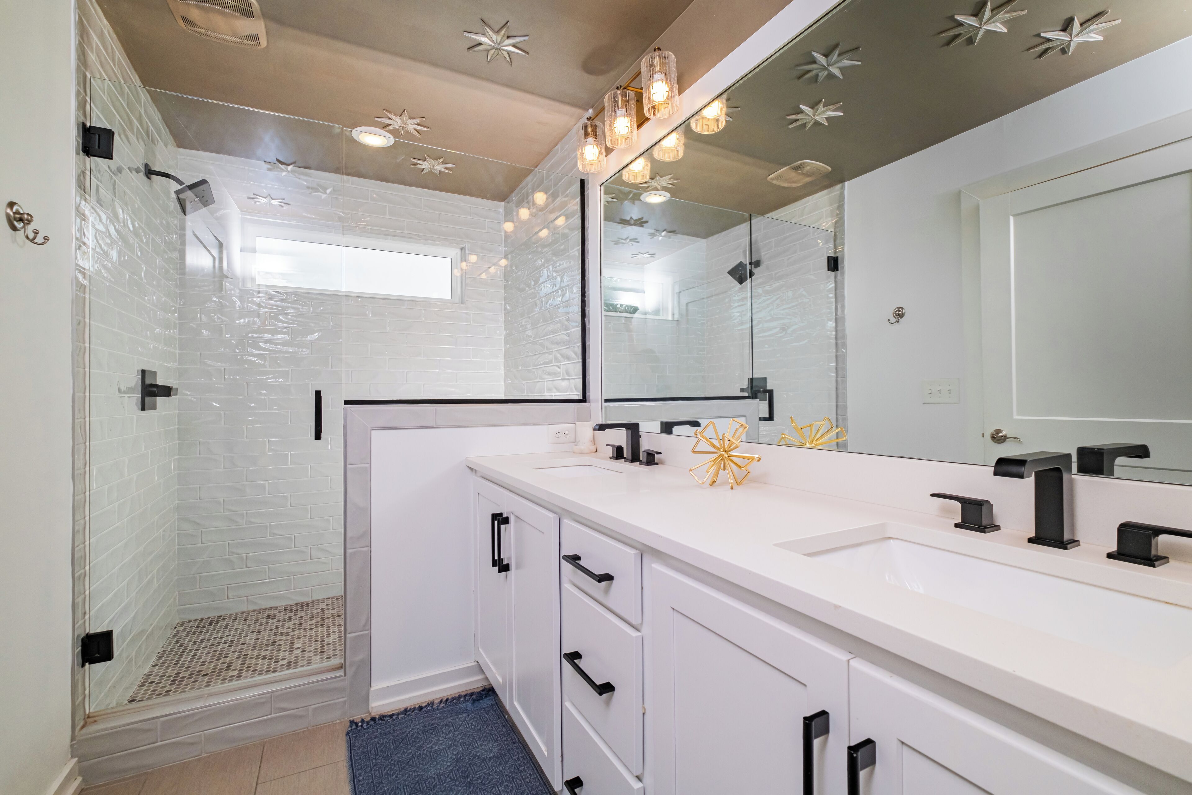 A modern bathroom with a glass shower enclosure, white cabinetry, and a large mirror.