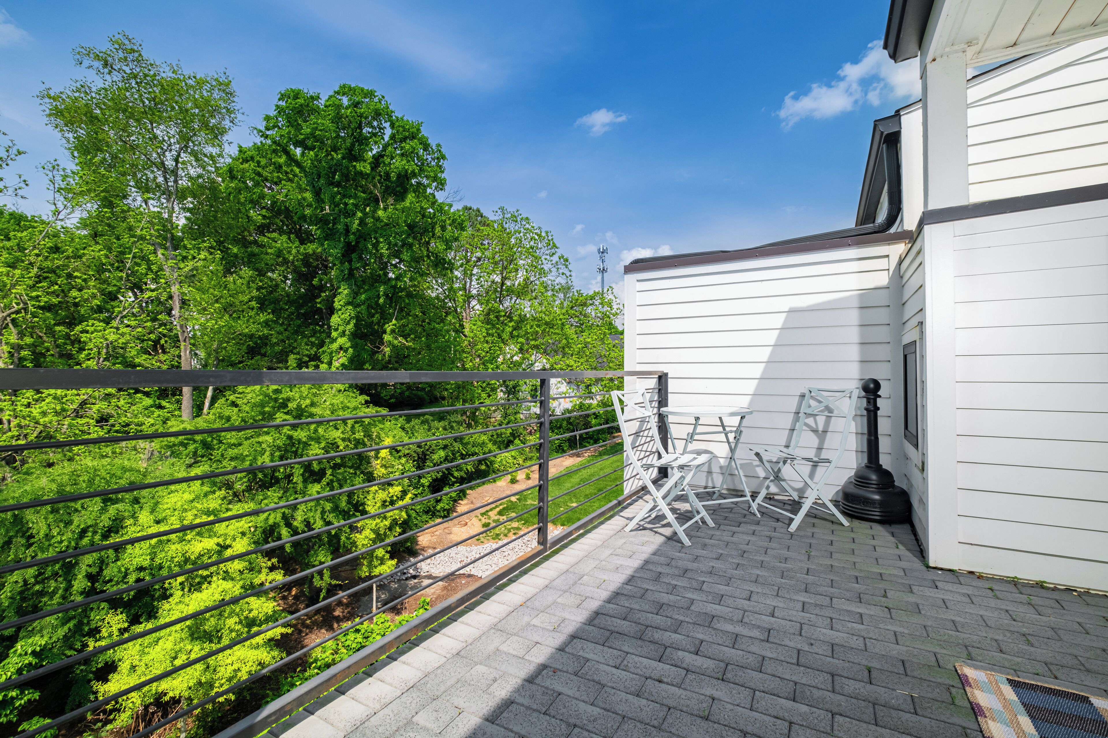 A balcony with a metal railing, white folding chairs, and a black lamp post.