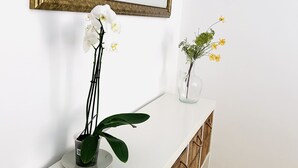 A white console table with a mirror above it, flanked by two potted plants with white and yellow flowers. - La Caracola (Benicarlo)