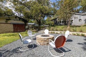 Une terrasse dotée d’un foyer en pierre et de quatre chaises, entourée d’une zone recouverte de gravier et d’arbres.