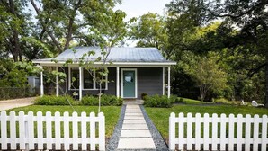 A single-story house with a covered porch, a gravel pathway leading to the front door, and a white picket fence. - Creek's Edge Peaceful Retreat with Firepit (Fredericksburg)