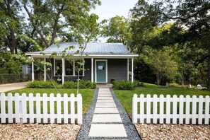 A single-story house with a covered porch, a gravel pathway leading to the front door, and a white picket fence.