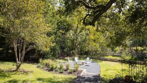 A backyard with a gravel path, white chairs, and a wooden deck. - Creek's Edge Peaceful Retreat with Firepit (Fredericksburg)