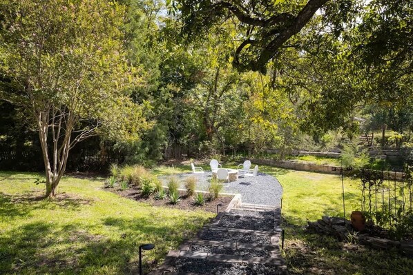 A backyard with a gravel path, white chairs, and a wooden deck.