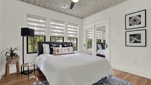 Un dormitorio con una cama grande, un ventilador de techo y dos ventanas con persianas.