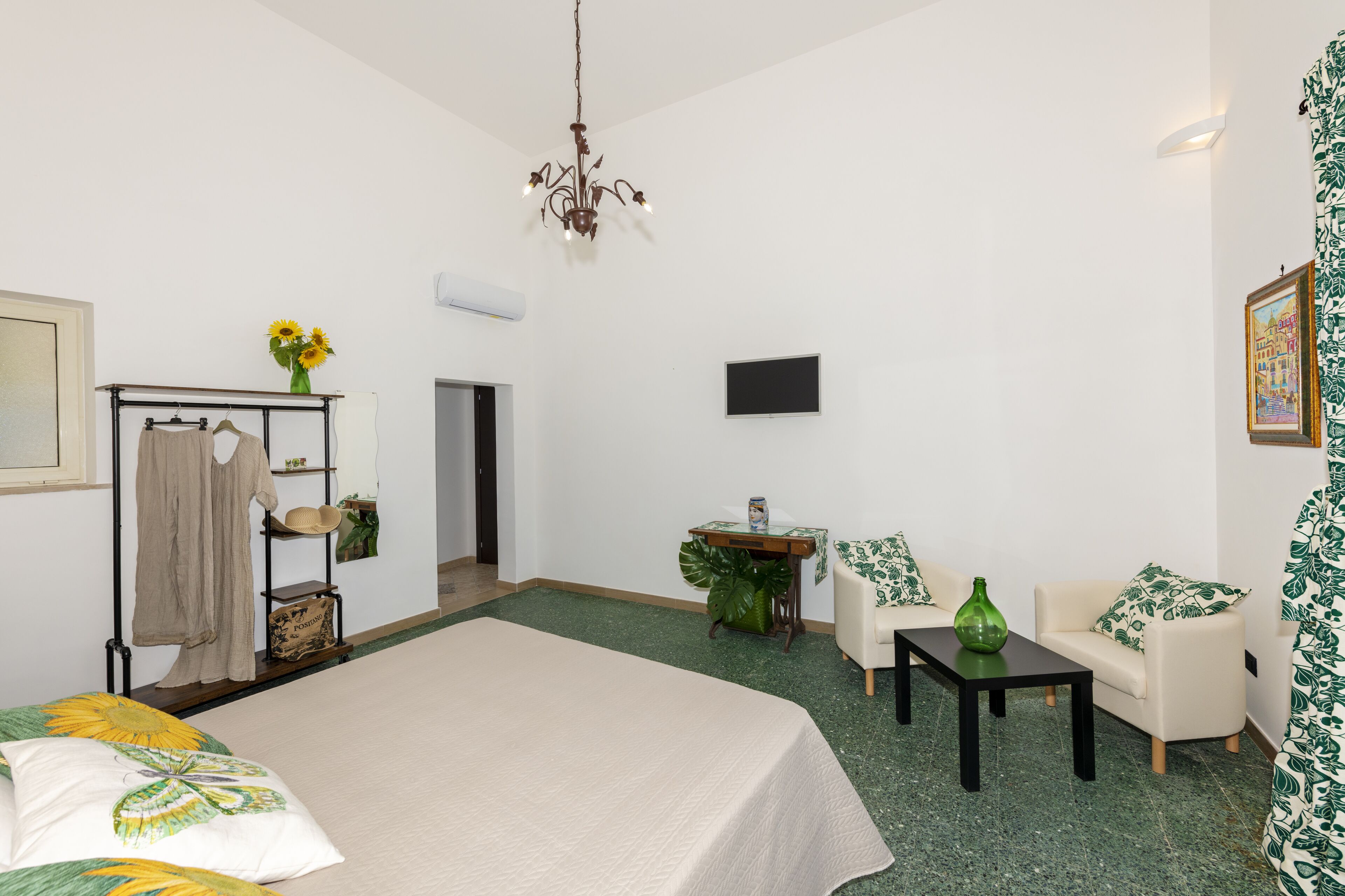 A hotel room with a bed, a small table, a sofa, a TV, and a chandelier.