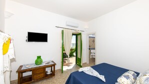 A bedroom with a bed, a TV, a small table with a vase, and a green door leading to an outdoor area. - YourHome - Casa Marina (Positano)