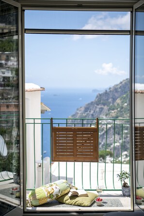 A balcony with a view of the sea, a wooden chair, a cushion, a potted plant, and a glass of wine. - YourHome - Casa Marina (Positano)