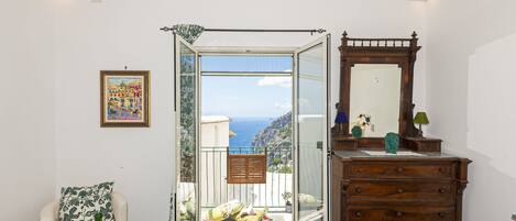 A room with a balcony, a wooden dresser, a framed picture, and a green vase on a table.