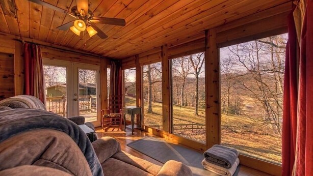 L’intérieur d’une cabane en bois comprend un lit, un ventilateur de plafond, une fenêtre donnant sur les arbres et une petite table.