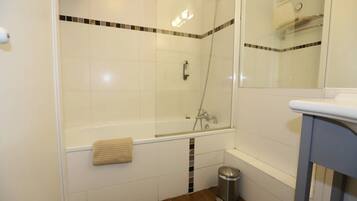 A bathroom with a glass-enclosed shower, a white bathtub, and a small trash bin.
