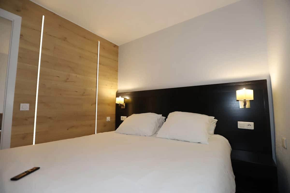 A hotel room with a large bed, wooden paneling on one wall, and two wall-mounted light fixtures.