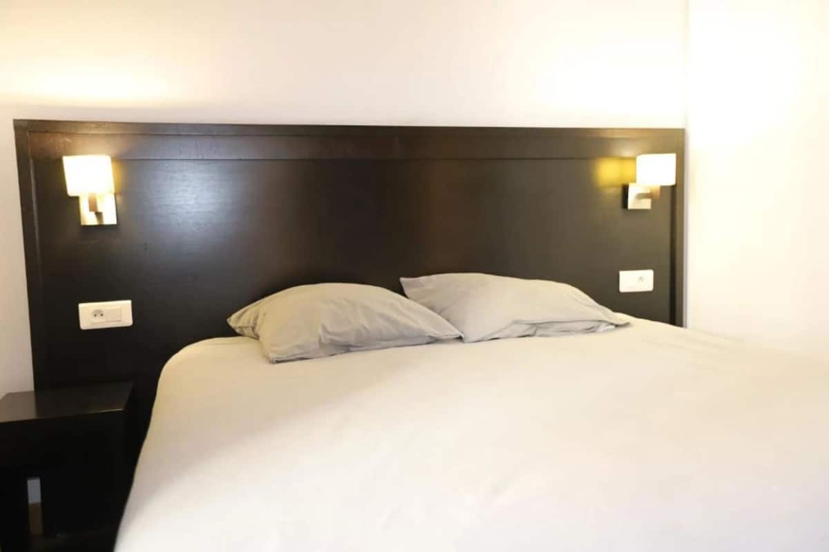 A hotel room with a dark headboard, two bedside lamps, and a bed with white bedding.