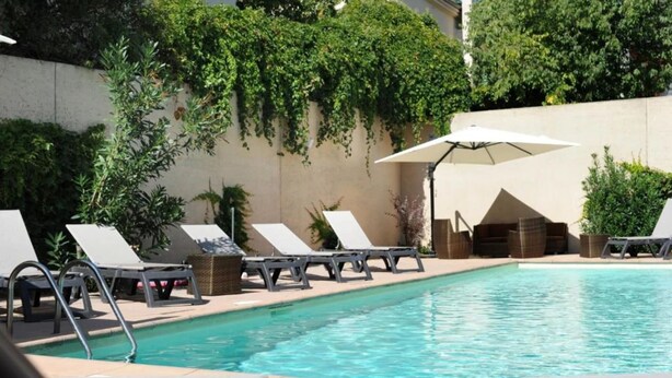 A pool area with lounge chairs and umbrellas, surrounded by greenery and a concrete wall. - Floridianes Provence (Aix-en-Provence)