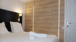 A neatly made bed with white linens, a wooden panel wall, and a bedside lamp. - Floridianes Provence (Aix-en-Provence)