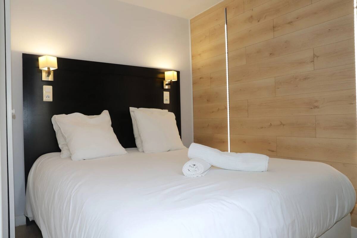 A neatly made bed with white linens, two wall-mounted light fixtures, and a wooden panel wall.
