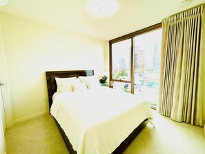 Ett hotellrum med en stor säng, ett fönster med gardiner och utsikt över stadsbilden.