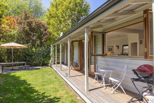 A covered outdoor area with a wooden deck, a barbecue grill, and a picnic table. - Stags head Cottage, Arrowtown Holiday Home (Arrowtown)