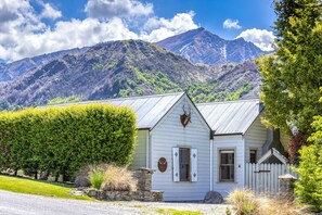 A white building with a metal roof, a stone wall, and a wooden fence. - Stags head Cottage, Arrowtown Holiday Home (Arrowtown)